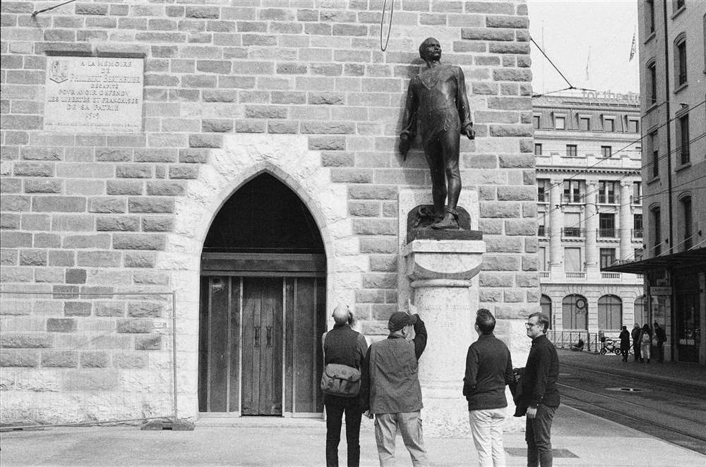 四个男人看着 Rue de la Tour-de-I'lle 和框架中的男人雕像。