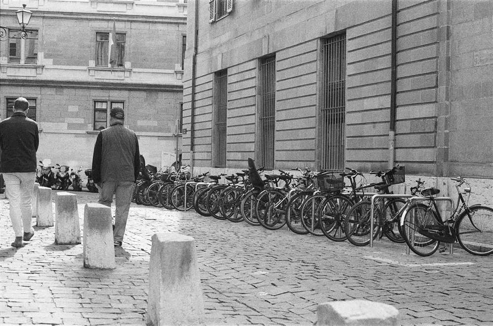 两名男子在街边骑着自行车走在街上。