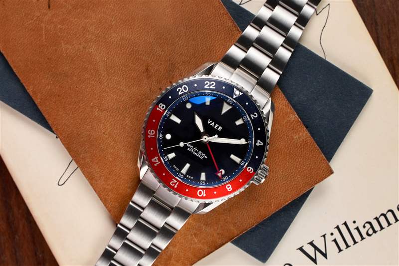 一块带有红色和蓝色表圈的 GMT 手表放在一块棕色皮革上。